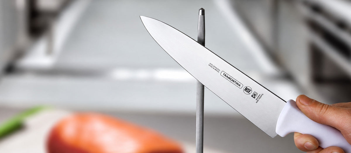 Cuchillo chef Tramontina Profissional Master con mango blanco y sello NSF, asentado con chaira en cocina profesional