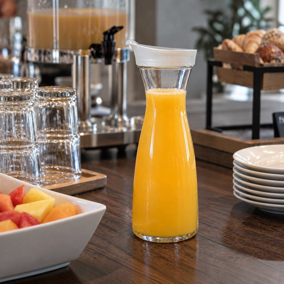 Decantador transparente Buffetware con tapa blanca, utilizado para servir agua en un vaso.